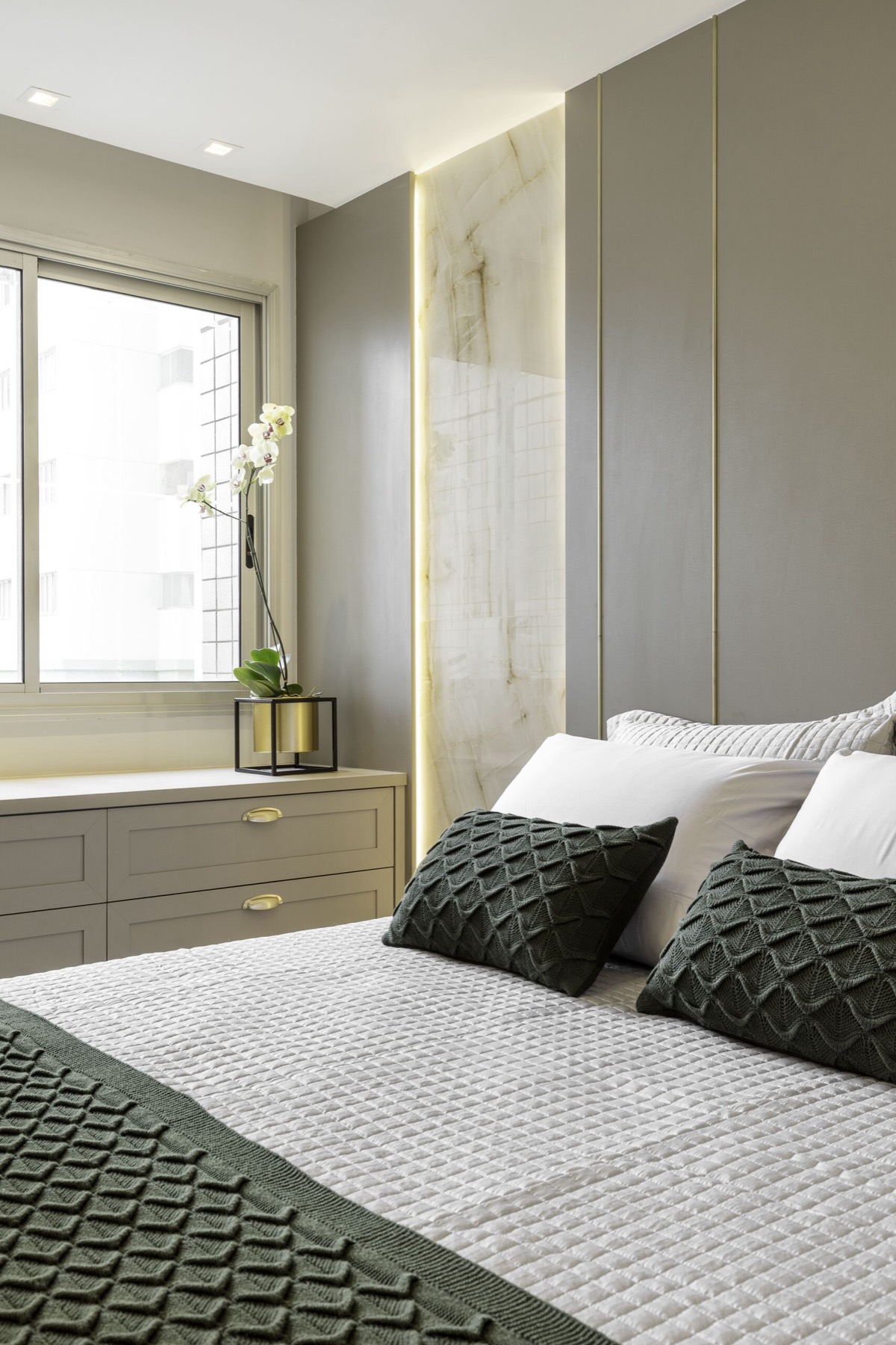 Suíte do Apartamento RAL com painel verde-oliva, nicho iluminado em mármore e roupa de cama em tons de verde
