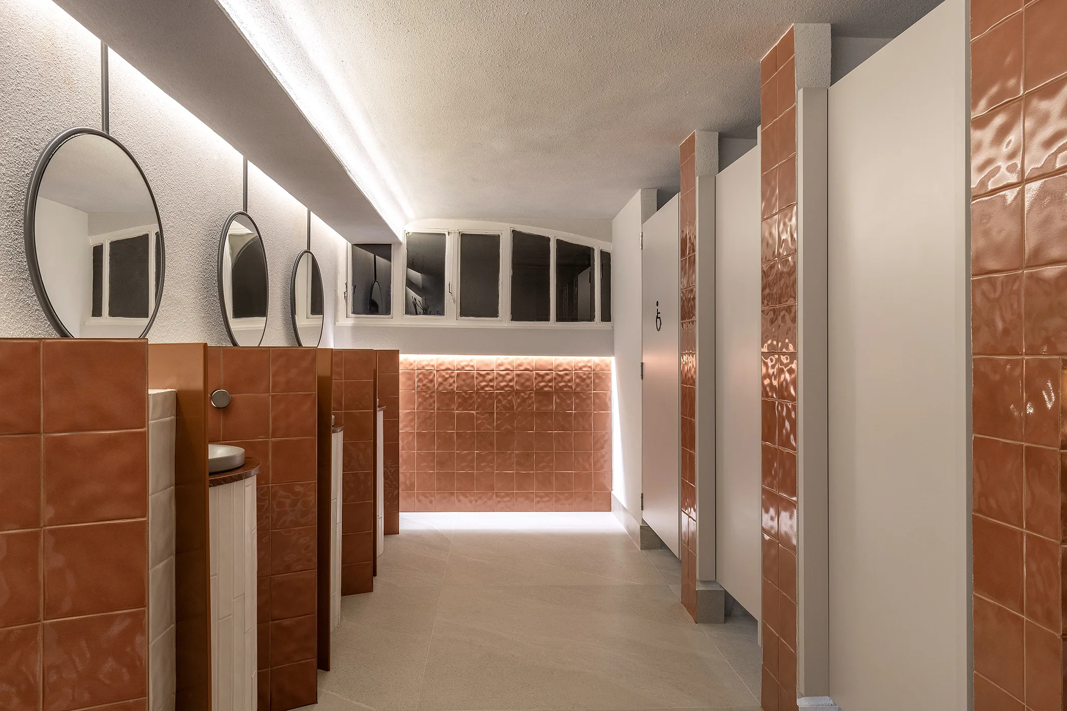 Lavabo Contratempo: bancadas e divisórias em porcelanato vermelho, cubas cilíndricas, espelhos redondos e iluminação indireta